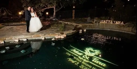 Bride and groom pose by illuminated pool.