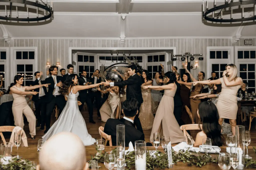 Wedding party dancing in formal attire indoors.