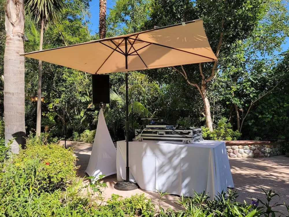 Outdoor DJ setup with umbrella in garden setting.