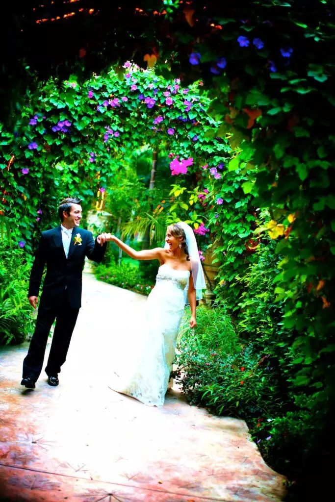 Bride and groom walking under floral archway.