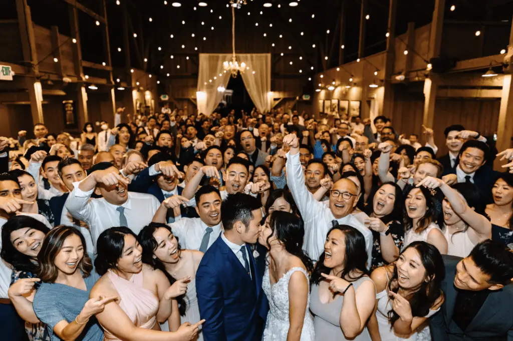 Happy wedding crowd celebrates bride and groom kissing.