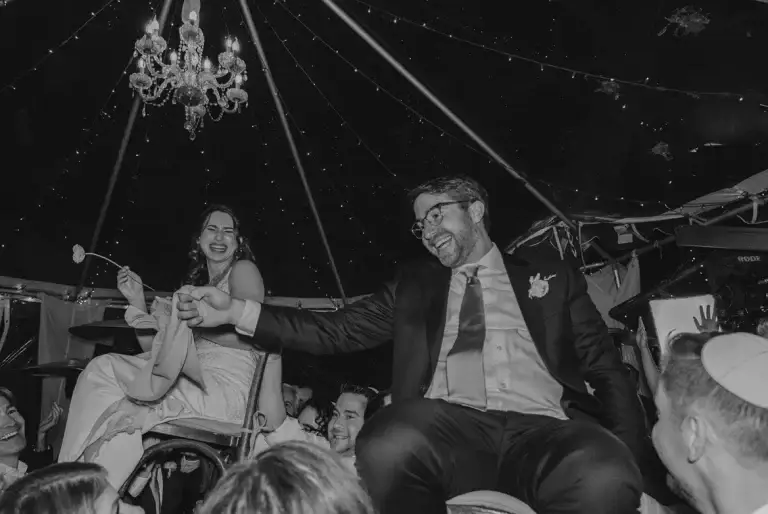 Couple celebrating on chairs during wedding reception.